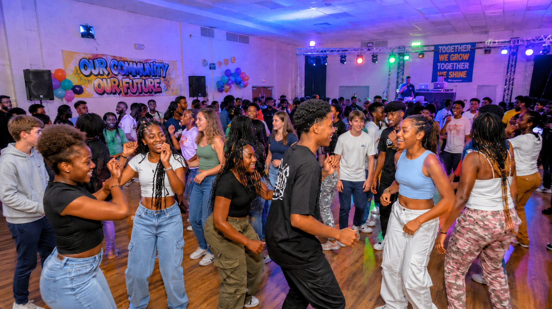 A packed hall of teenagers and young adults dancing under colourful stage lights at an Afro Youth Dance night